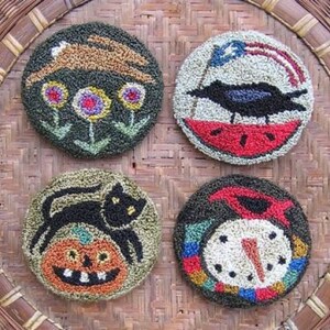 May include: Four round needlepoint embroidery hoops with different seasonal designs. The top left hoop features a brown rabbit under a green bush with three yellow, purple, and green flowers. The top right hoop features a black bird with a red, white, and blue watermelon slice. The bottom left hoop features a black cat with a jack-o-lantern. The bottom right hoop features a snowman with a red hat and a blue scarf.