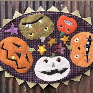 May include: A purple and white patchwork fabric with a variety of Halloween-themed appliques, including pumpkins, a ghost, and stars. The fabric is stitched together in a circular shape with a scalloped edge.