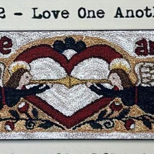 May include: A rectangular rug with the text "Love One Another" above a design featuring a heart, angels, and floral elements. The heart is red and white, with angels on either side. The rug has a black border.