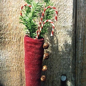 May include: A red felt stocking with a green toe, filled with candy canes and decorated with jingle bells. The stocking is hanging on a wooden wall.