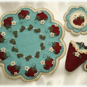 May include: A set of three felt needlepoint pieces featuring a strawberry theme. The set includes a round table runner, a smaller round coaster, and a strawberry-shaped needlepoint holder with a drawstring.