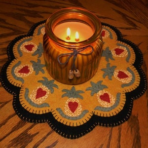 May include: A yellow felt pineapple-themed candle mat with a black border and a glass candle jar with a brown lid and a brown ribbon.