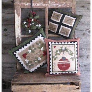 May include: A rustic wooden chair displays four decorative Christmas pillows. The pillows feature festive designs, including a red ornament, mistletoe, and the words "Joy" and "Peace". The pillows are in shades of green, red, and beige.