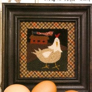 May include: A framed needlepoint design featuring a white chicken with a red comb, standing in front of a red barn. The background is a brown and tan plaid pattern.