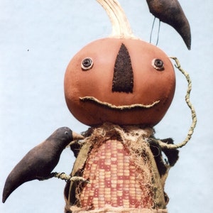 May include: A handmade pumpkin doll with a stitched-on face and two black crows perched on its head and arm. The doll is dressed in a brown fabric with a corn husk pattern and a burlap sash.