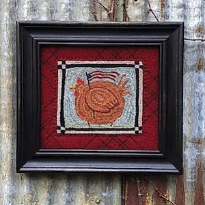 May include: A framed needlepoint artwork featuring a brown chicken with a small American flag on its head. The background is a red and white checkered pattern.