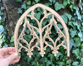 Puede incluir: Un recorte de madera de una ventana de arco gótico con detalles intrincados. El arco está hecho de madera fina y tiene un color marrón claro.