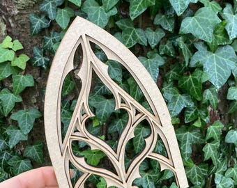 Puede incluir: Un recorte de madera de una ventana de arco gótico con intrincados detalles. El recorte está hecho de madera marrón claro y tiene un acabado natural.