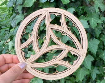 Puede incluir: Un posavasos redondo de madera cortada con láser con un diseño intrincado y en capas. El posavasos presenta un patrón repetitivo de formas arqueadas y motivos florales, creando una pieza decorativa y artística. El color natural de la madera contrasta con las líneas de corte oscuras.