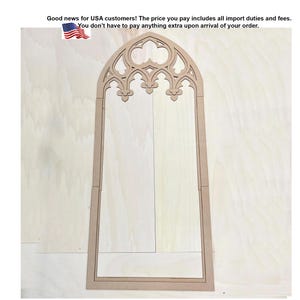 May include: A light brown wooden cutout in the shape of a tall, arched window frame. The top section features intricate, decorative gothic-style tracery with pointed arches and trefoil elements, while the lower portion consists of a simple rectangular frame.