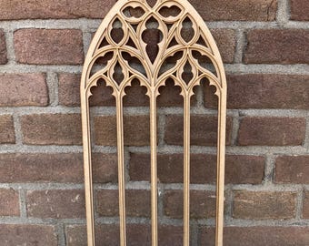 Puede incluir: Un recorte de madera de una ventana de arco gótico con detalles intrincados. La ventana está hecha de múltiples paneles con un diseño decorativo.