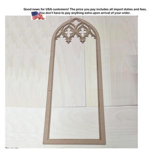 Op de afbeelding: Een hoog, lichtgekleurd houten frame met een spitsgotische boog aan de bovenzijde. Het bovenste gedeelte bevat ingewikkelde, symmetrische uitgesneden patronen. Het frame heeft een rechthoekige basis en een gladde afwerking.