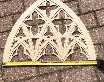 Puede incluir: Un marco de ventana gótica de madera sin terminar de color marrón claro con intrincados diseños recortados. El marco mide aproximadamente 61 cm de ancho, con una cinta métrica al lado. El diseño presenta formas arqueadas y patrones en forma de cruz.