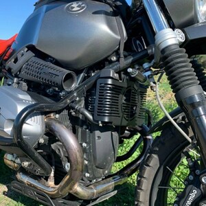 May include: Close-up of a gray and black motorcycle. The fuel tank has a BMW logo. The exhaust pipe is silver. The front tire has a Brembo brake. The motorcycle is parked on grass.