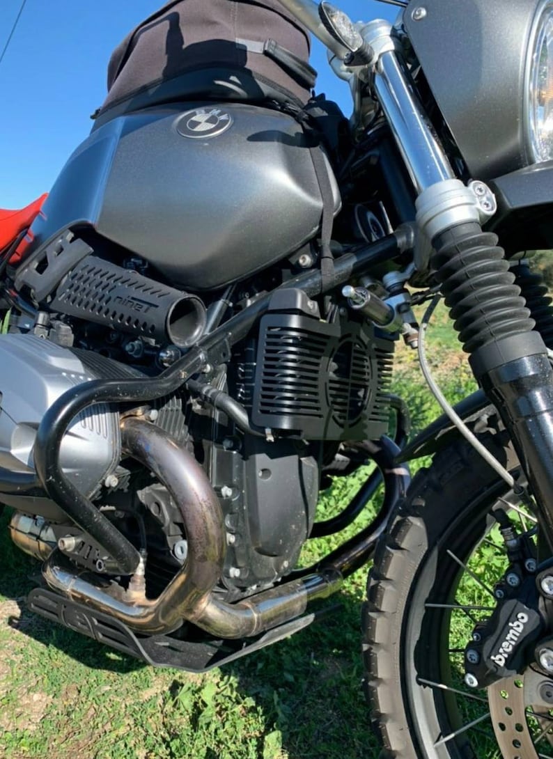 May include: Close-up of a gray and black motorcycle. The fuel tank has a BMW logo. The exhaust pipe is silver. The front tire has a Brembo brake. The motorcycle is parked on grass.