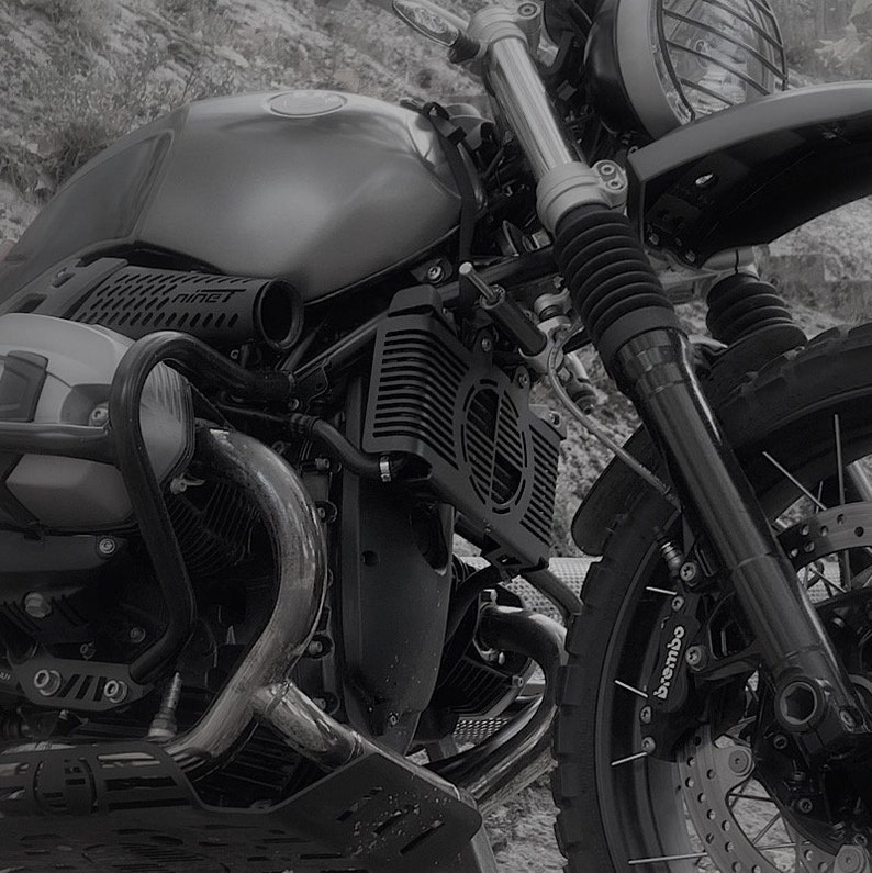 May include: A grayscale image of a motorcycle, showcasing its front section. The motorcycle features a round headlight, a fuel tank, and a prominent engine with a radiator. The front suspension and a Brembo brake caliper are also visible.