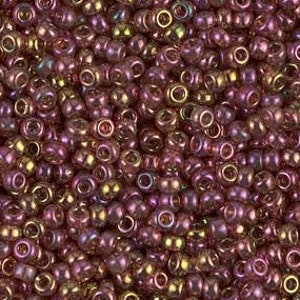 May include: A close-up view of a large quantity of small, round, iridescent beads. The beads are a deep purple color with a gold sheen.