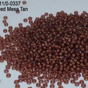 以下が含まれることがあります： たくさんの小さな茶色のガラスビーズの山。ビーズは半透明で、わずかに光沢があります。ビーズには「Item: RR11/0-0337 Inside Dyed Mesa Tan」とラベルが貼られています。