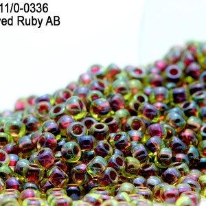 May include: A close-up of a pile of small, iridescent glass beads. The beads are a mix of green, red, and gold colors. The beads are in a clear container, and the text "Item: RR11/0-0336 Inside Dyed Ruby AB" is visible in the top left corner of the image.