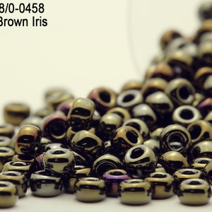 May include: A close-up of a pile of metallic brown iris seed beads. The beads are small and round, with a shiny finish. The beads are arranged in a loose pile, and some of the beads are overlapping.