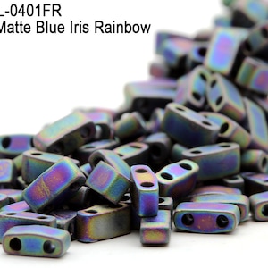 Puede incluir: Un montón de cuentas de semillas de dos agujeros de color azul irisado mate metálico. Las cuentas son pequeñas y rectangulares con una ligera curva. Las cuentas son iridiscentes y tienen un color azul, morado y verde.