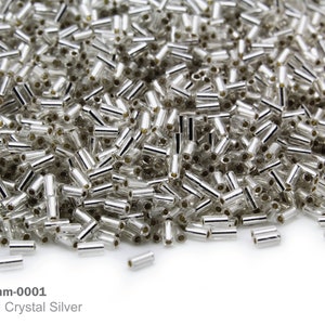 Op de afbeelding: Een close-up afbeelding van een stapel zilveren kristallen kralen. De kralen zijn klein en cilindrisch, met een zilveren coating aan de buitenkant. De kralen zijn in een willekeurig patroon gerangschikt, en sommige overlappen elkaar. Artikel: RB 3mm-0001 Zilveren kristallen kralen met een zilveren coating