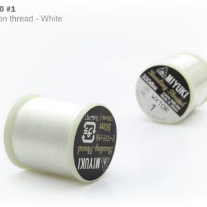 May include: Two spools of white Miyuki nylon beading thread. The spools have black and white labels with text that includes "Miyuki" and "Beading Thread". The thread is 50m in length.