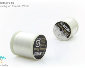 Può includere: Due rocchetti di filo di nylon bianco Miyuki per perline. Le bobine hanno etichette in bianco e nero con testo che include "Miyuki" e "Beading Thread". Il filo è lungo 50 m.