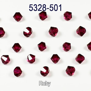 Puede incluir: Una vista de cerca de 20 cuentas de cristal de color rojo rubí. Las cuentas son facetadas y tienen un acabado brillante. Las cuentas están dispuestas en un patrón de cuadrícula sobre un fondo blanco. El texto "5328-501" y "Ruby" es visible en la imagen.