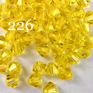 May include: A close-up image of a large quantity of small, faceted, yellow glass beads. The beads are arranged in a random pattern and have a shiny, reflective surface. The number 226 is visible in the image.
