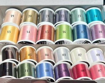 May include: A collection of colorful spools of thread, arranged in a box. The threads are in various shades, including pink, gold, blue, green, and purple. Each spool is labeled with a number.