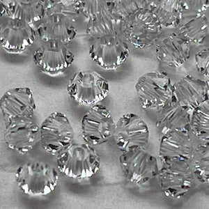 May include: A large quantity of clear glass beads with a faceted, starburst design. The beads are scattered on a white surface.