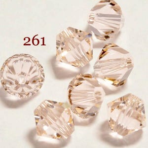 May include: A group of seven clear pink glass beads with a faceted design. The beads are approximately 10mm in diameter. The beads are arranged in a random pattern on a white surface. 261