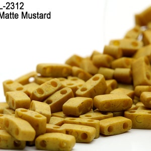 May include: A close-up of a pile of opaque matte mustard colored plastic beads. The beads are rectangular with two holes in each. The beads are spilling out of a clear container.