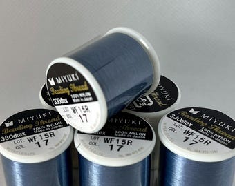 May include: Several spools of Miyuki Beading Thread in a deep blue color. Each spool has a white label with black text indicating the thread type, lot number, and that it is made of 100% nylon. The spools are stacked and arranged.