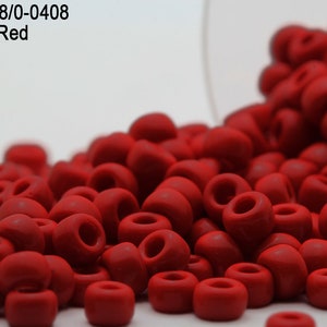 May include: A close-up of a pile of opaque red round beads. The beads are small and have a smooth, matte finish. The beads are spilling out of a clear container.