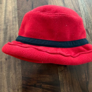 Könnte beinhalten: Ein roter Fleece-Bucket-Hut mit einem schwarzen Band um die Krone.