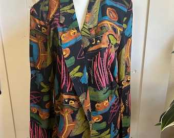 May include: A black blazer with a vibrant abstract pattern in shades of orange, teal, pink, and green. The blazer features a classic lapel and long sleeves, displayed on a mannequin. The design is reminiscent of an artistic painting.