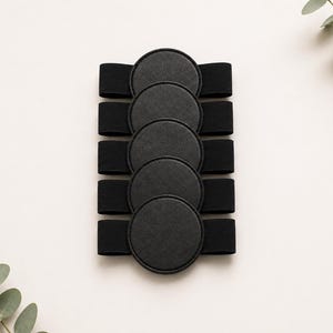 May include: A set of five black circular patches, each attached to a horizontal black elastic band. The patches are arranged in a vertical column, featuring a smooth, matte texture with stitched edges, creating a uniform and functional design.