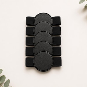 May include: A set of five black circular patches, each attached to a horizontal black elastic band. The patches are arranged in a vertical column, featuring a smooth, matte texture with stitched edges, creating a uniform and functional design.