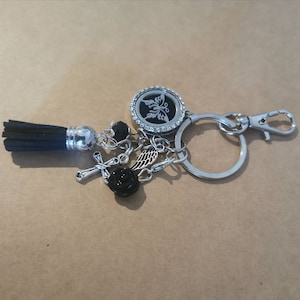 Può includere: Un portachiavi argentato con un nappa nera, un ciondolo a forma di rosa nera, un ciondolo a forma di croce, un ciondolo a forma di ala d'angelo argentata e un ciondolo argentato con un design a forma di farfalla e strass.