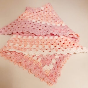 May include: A pink and white crocheted baby blanket with a scalloped edge.