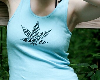 May include: A light blue sleeveless vest top featuring a black and white zebra-striped leaf graphic on the front. The garment has a scoop neckline and is constructed from a solid-coloured fabric. The design is centred on the chest area of the top.