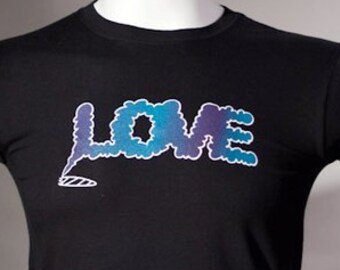 May include: A black short-sleeve t-shirt featuring the word LOVE printed in a blue and purple gradient cloud-like font. Below the letter L, a small white outline of a smoking cigarette is visible on the chest of the garment.