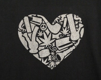 May include: A black short-sleeved t-shirt featuring a large, silver glitter heart graphic on the chest. The heart design is composed of various icons, including cannabis leaves, smoking pipes, and peace symbols, arranged in a collage pattern.