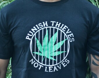 May include: A black short-sleeve t-shirt featuring a circular graphic with white vertical bars resembling a cage. Inside the cage is a green cannabis leaf. The text "PUNISH THIEVES NOT LEAVES" is printed in white in a circular arc around the cage.