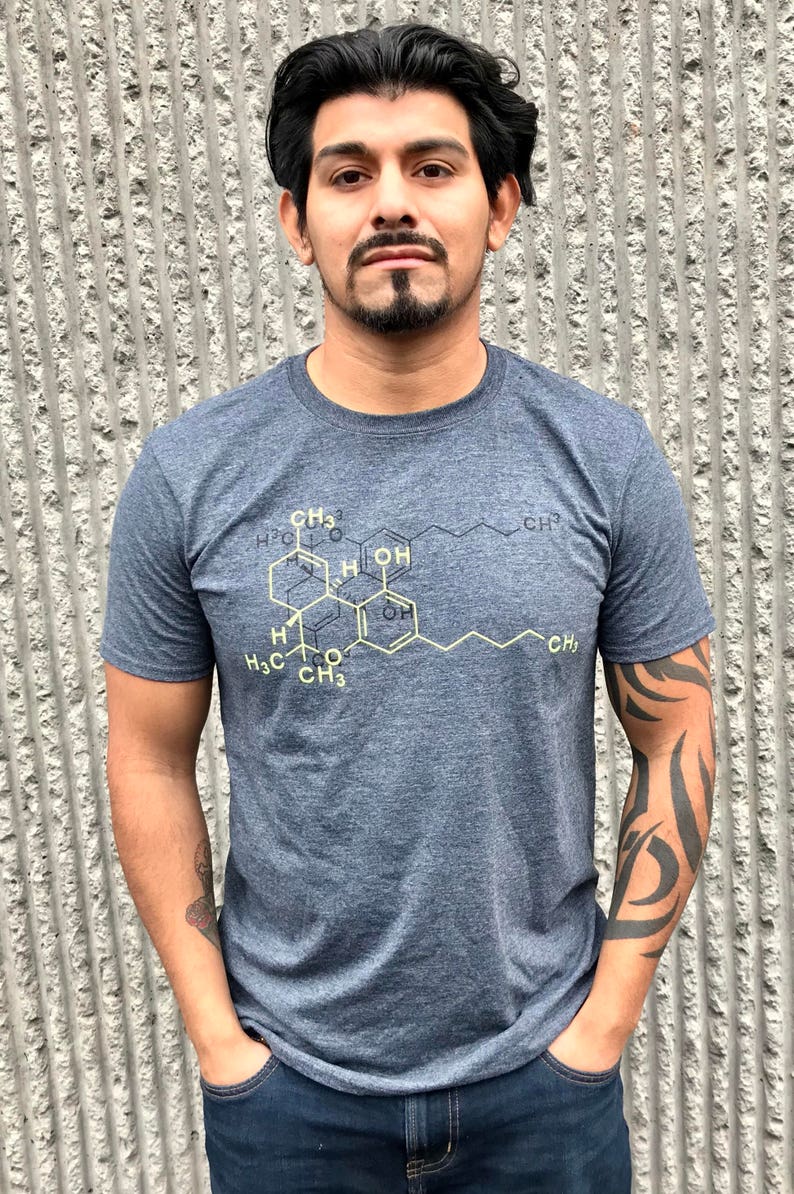 May include: A heathered dark blue short-sleeve t-shirt featuring a yellow chemical structure diagram printed on the chest. The graphic displays a complex molecular formula with various carbon and hydrogen labels, including CH3 and OH groups.