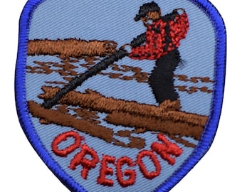 May include: A shield-shaped embroidered patch with a light blue background and a dark blue border. It features a figure in a red and black plaid shirt and black pants using a chainsaw on a brown log. The word OREGON is stitched in red letters.