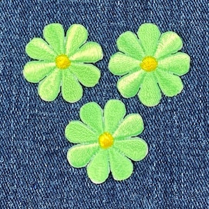 May include: Three green felt flower patches with yellow centers. The patches are on a blue denim background.
