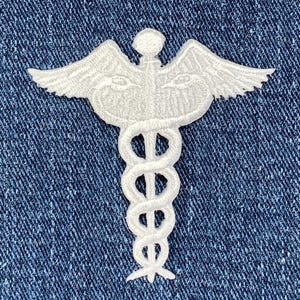 May include: White embroidered medical symbol patch with a snake wrapped around a staff and wings on a blue denim background.